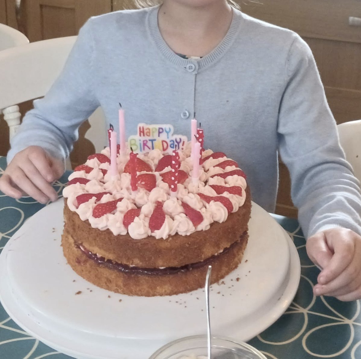 A homemade Victoria sponge birthday cake topped with strawberries, piped cream and lit candles